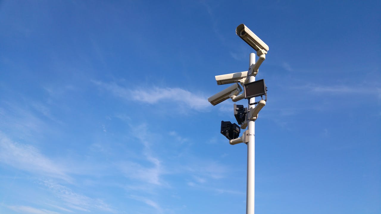 Multiple security cameras on a pole with a clear blue sky backdrop.