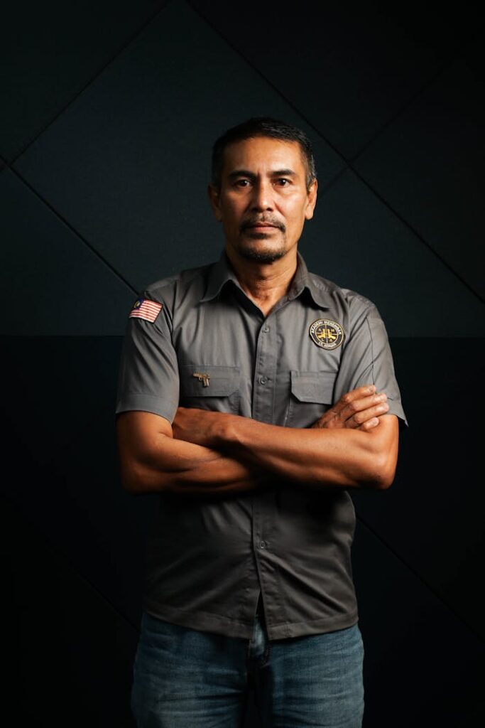 Portrait of a confident adult security guard in uniform with arms crossed, indoors.